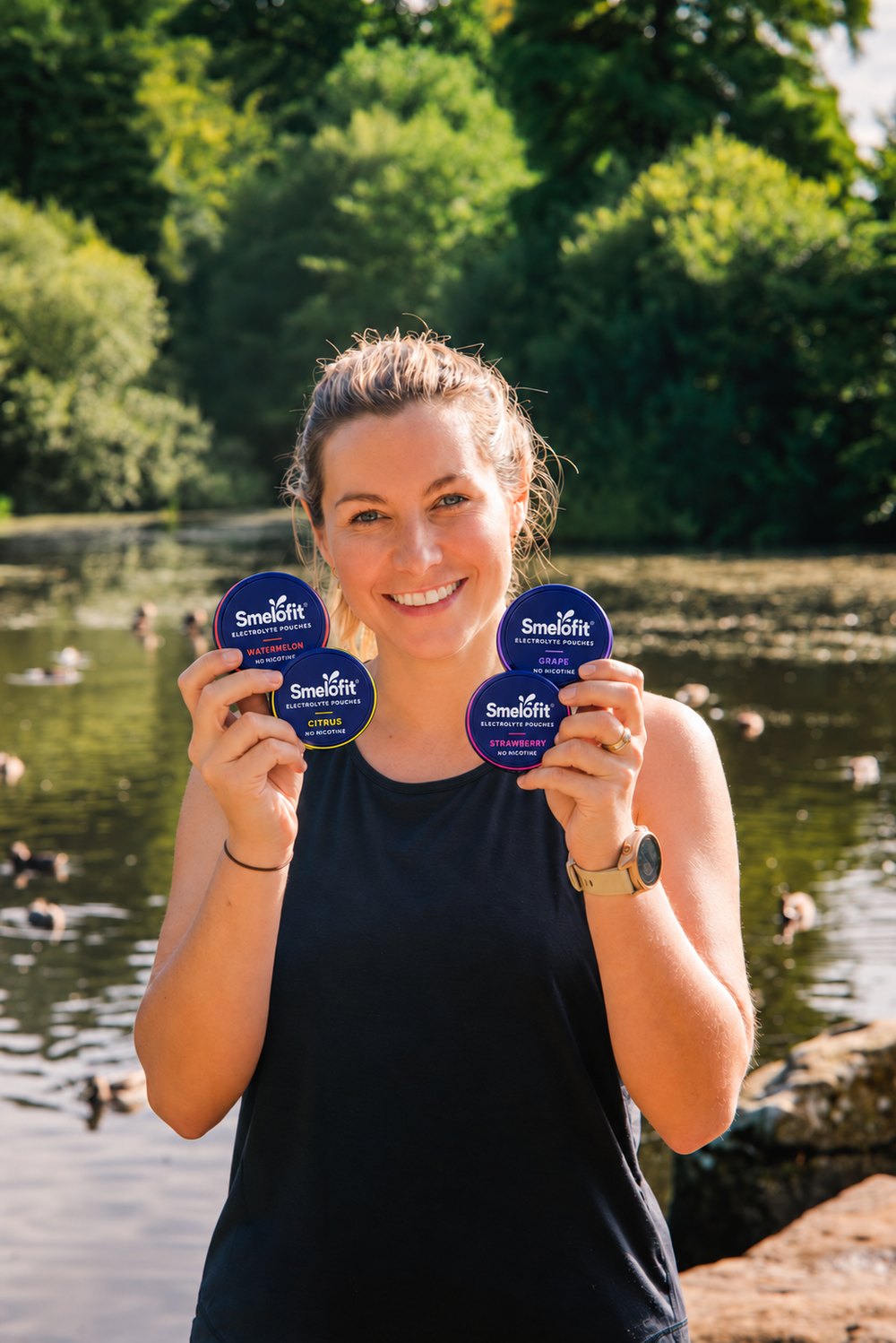 A smiling woman holding four smelo tins by the lake